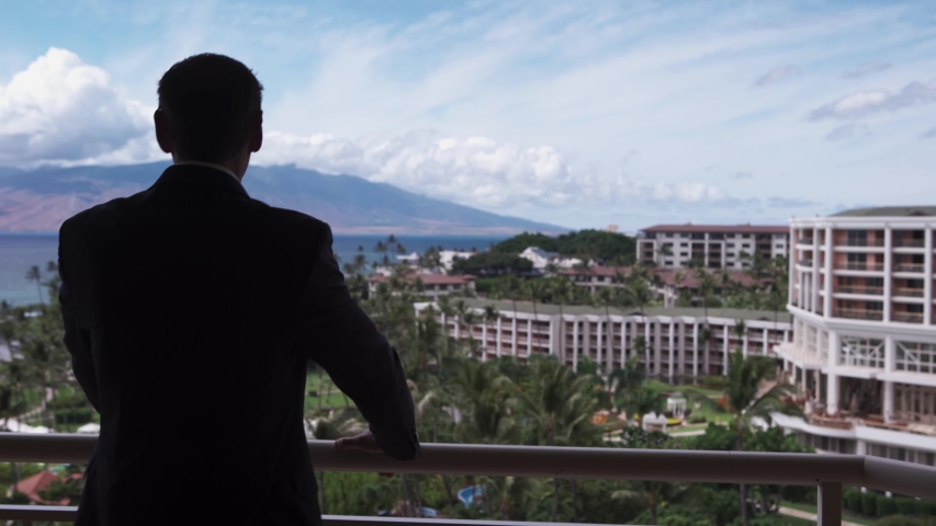 Businessman stares at luxurious hotel coastline in Maui Hawaii. 