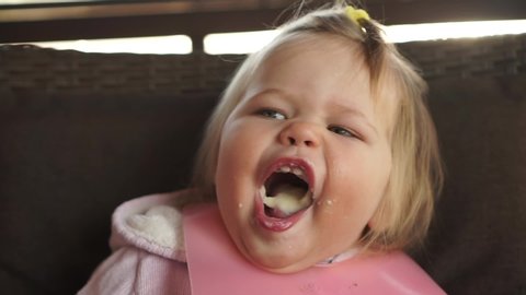 Little chubby baby girl hilariously open mouth full of milk food eating very good appetite feeding from spoon