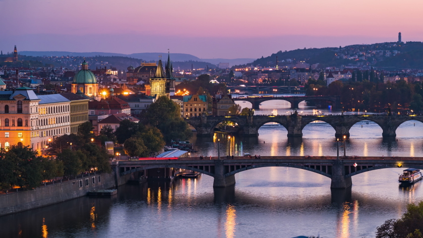 Prague, Czech Republic, dolly right timelapse sequence showing Prague cityscape with medieval bridges and boats on the Vltava river at dusk. 