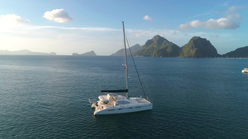 Aerial drone view of sailing yacht anchored in the bay with clear and turquoise water on the sunset. Sailing yacht in the tropical lagoon. Tropical landscape. El Nido, Palawan island, Philippines. Royalty-Free Stock Footage #1056070961