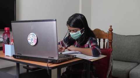 Indian Girl learning online wearing protective face mask during Corona virus pandemic or COVID-19 spread in India. kid using laptop attending online class.