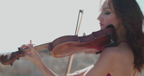 Close portrait of female violinist plays instrumental music, then camera changing view on other woman among the spacious cliffs in sunny summer. Slowly in 4K