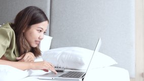 Young Asian woman using laptop for studying on the bed. New normal concept.