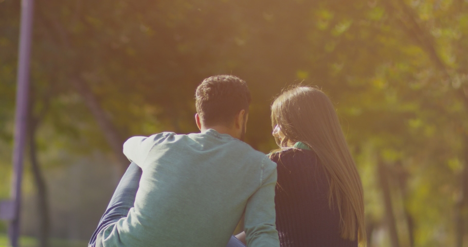Back view of happy lovely caucasian romantic couple sitting on lawn and hugging each other in park . Rear view of young couple sit on grass and enjoy in the open air. Happiness people . Slow Motion . | Shutterstock HD Video #1056076127