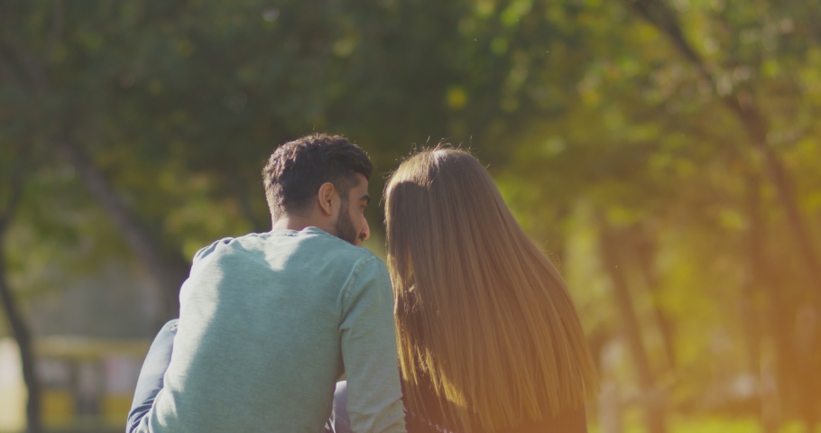 Back view of happy lovely caucasian romantic couple sitting on lawn and hugging each other in park . Rear view of young couple sit on grass and enjoy in the open air. Happiness people . Slow Motion . | Shutterstock HD Video #1056076130