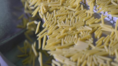 Close up slow motion of raw dried organic penne macaroni running on a steel conveyor belt in an Italian pasta factory. Healthy food.