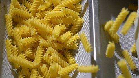 Overhead of raw dried organic pasta rotini macaroni running on a steel conveyor belt in an Italian pasta factory. Healthy fusilli. Food.