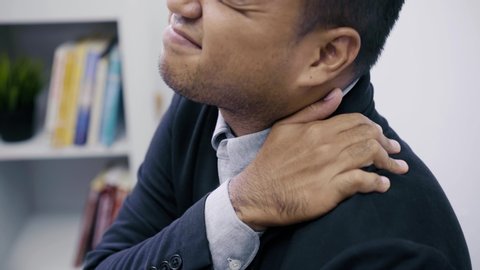 Office syndrome concept, Asian businessman works at computer, he experiences pain in neck and touches his neck with one hands, turns his head in attempt to relieve pain. 4k Resolution.