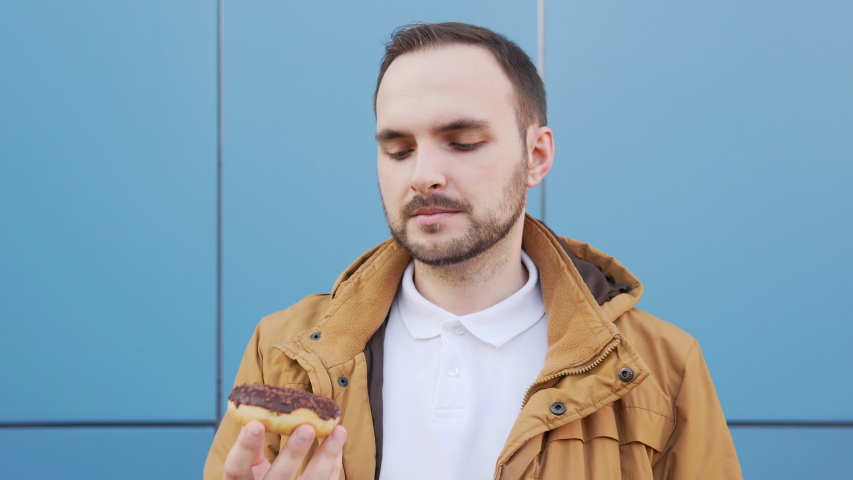 Bearded man sniffs a chocolate donut and admires its aroma. ProRes codec. Close up shot, 4k. Royalty-Free Stock Footage #1056079046