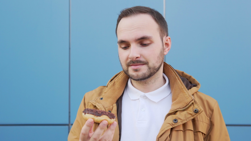 Bearded man sniffs a chocolate donut and admires its aroma. ProRes codec. Close up shot, 4k. | Shutterstock HD Video #1056079046