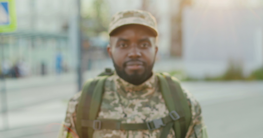 Portrait shot of smiling African American young male soldier in cap with backpack smiling to camera at street. Going to army. Royalty-Free Stock Footage #1056080630