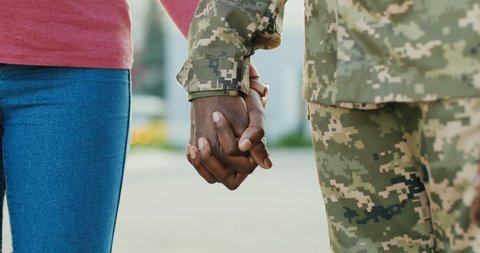 Close up of African American male and female hands holding each other gently outdoors. Man soldier in military uniform taking hand of woman, his girlfriend or wife. Happy meeting concept.