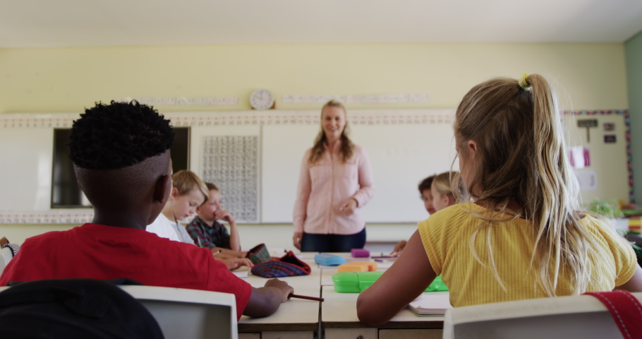 Multi-ethnic group of children and their Caucasian female teacher sitting in a classroom during a lesson, children raising their hands, in slow motion. Education at an elementary school. Royalty-Free Stock Footage #1056081932