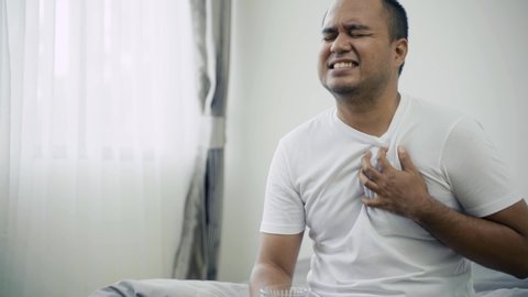Asian sick person has pain in chest while he drink water, He has difficulty breathing or pain in chest touches chest with his hand. Panic attack, white shirt man get hurt and he sick. 4k Resolution.