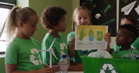 Multi-ethnic group of children wearing green t shirts with a white recycling logo, holding a poster about recyclable materials, in slow motion. education at an elementary school.