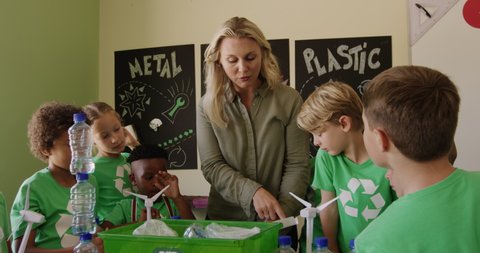 Multi-ethnic group of children wearing green t shirts with a white recycling logo and their Caucasian female teacher discussing recyclable materials, in slow motion. Education at an elementary school.