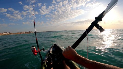 Kayak fishing, trolling fishing. Fisherman trolling in kayaks at mediterranean sea on a windy day with waves during sunset. Aquatic summer sports. Kayaker trolling and fishing at sea in his canoe. 