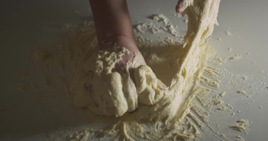 Female hands kneading dough in flour on the white table, slow motion, single light illuminates the scene. | Shutterstock HD Video #1056082943