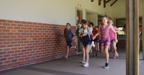 Multi-ethnic group of children wearing backpacks, running in an outdoor corridor during break, in slow motion. Education at an elementary school.