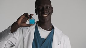 Young attractive cheerful African American male doctor happily holding antiseptic bottle over gray background