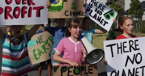 Multi-ethnic group of children walking down a road on a protest march, carrying signs with environmental and conservation slogans, in slow motion. Elementary school children ecology awareness protest.