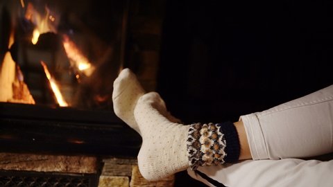 Person sitting warming their feet near fireplace wearing woolen socks. Cozy home footage, Christmas concept, old-fashioned concept. Arkivvideo