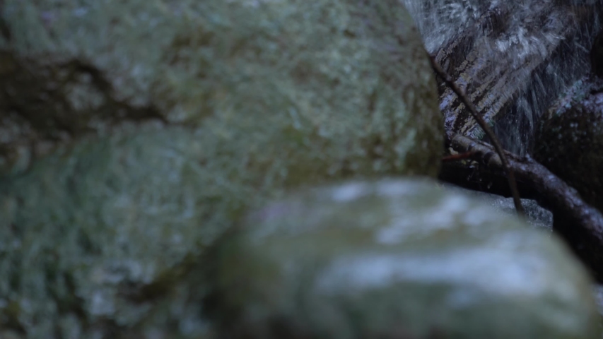 Close up vertical pan of white water flowing over the rocky surface of a man made waterfall cascade with wet slippery boulder rocks covered in dark green algae in the foreground.