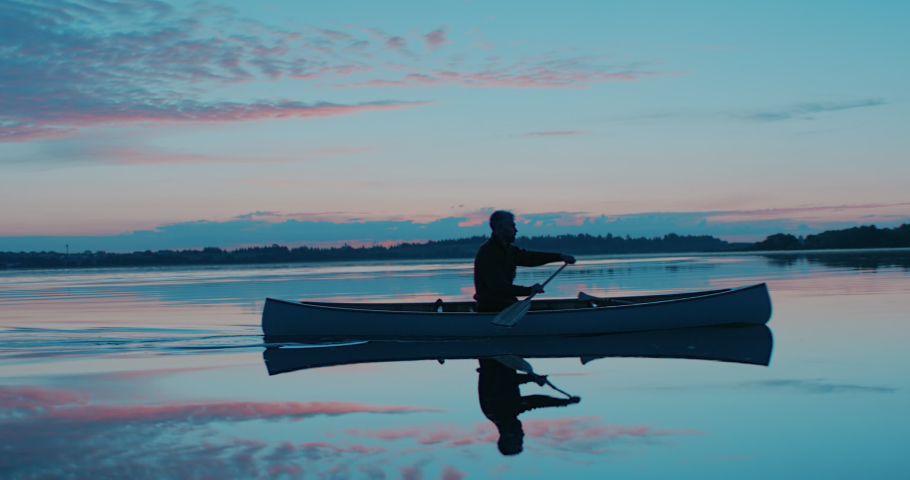 Man canoeing in a traditional wooden boat on a large lake at dawn. Shot on RED cinema camera with 2x anamorphic lens