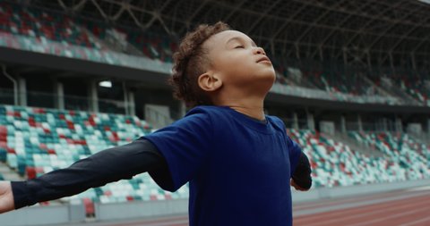 Portrait of cute little black kid spreading hands on a large football stadium, dreaming of becoming professional player, soccer star. Shot on RED camera with anamorphic lens