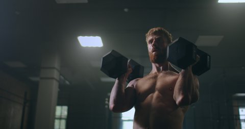 a powerful and strong athlete pushes dumbbells standing in the gym in slow motion.