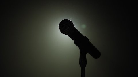 Close-up of microphone on stage against a black background with white lighting and smoke. The silhouette of the microphone in the dark. Music instrument concept.