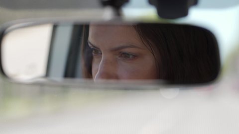 Beautiful brunette woman reflected in rearview mirror closeup, woman driving car, rear view of woman drives automobile through the city streets.