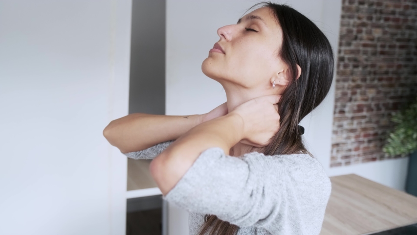 Video of tired young woman suffering neck pain while sitting on the stool in the kitchen at home. Royalty-Free Stock Footage #1056098183