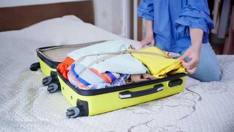 luggage for vacation, young woman is going to travel and trying to close her suitcase with things and clothes, sits on top and zips up on her travel bag while sitting on bed in room