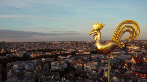 Flying over beautiful old town of Riga, Latvia at sunset with Domes cathedral and golden cock statue in the foreground. 