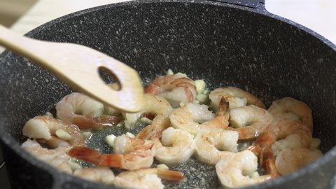 Chef cooks shrimps and garlic in a black frying pan