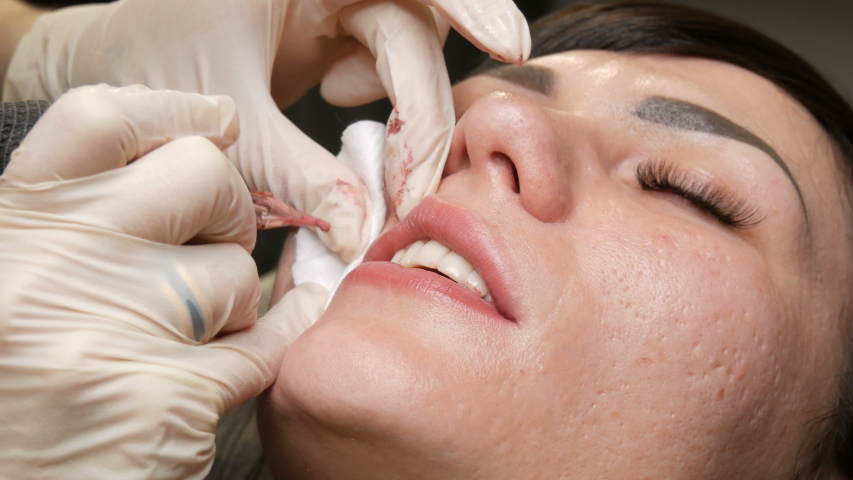Microblading lip tattoo with special coloring pigment that corrects lip color in cosmetology clinic. Hand makes permanent makeup lips procedure applying pigment makeup on lips with tattoo machine
