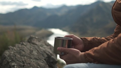Close up of hands of tourist traveler man with mug traveling on mountain, hiker man holding cup of tea. Active lifestyle hiking enjoying vacation travel tourism adventure landscape nature. 4 K slow-mo