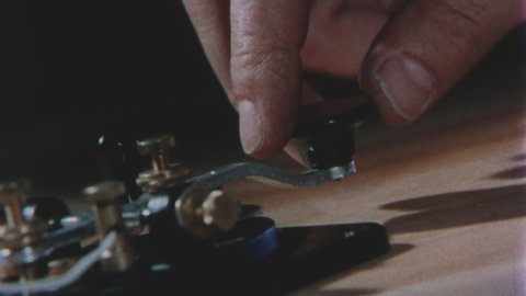 1940's USA. Extreme Close Up of Hand tapping out Morse code on a Telegraph Key. 4K Scan of Vintage 16mm Film Print.