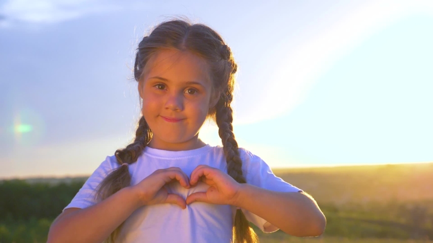 Happy little girl hands holding heart shape. Child at sunset folded his hands in form of heart. Girl smiles. Child love symbol of happy family. Heart sign of family love. Heart from hands, happy