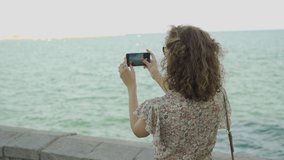 Tourist woman using smartphone and taking a photo of beautiful mediterranean sea in Sitges, Barcelona, Spain.Travel, tourism, summer holidays, active lifestyle concept