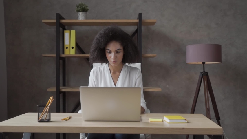Confused young african American girl sit at desk look at laptop screen, frustrated female feel mad dissatisfied experience from what he saw or data loss working on computer | Shutterstock HD Video #1056119606