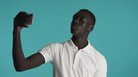 Young confident African American man turning head around taking selfie on smartphone over colorful background. Peace gesture