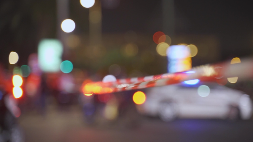Police red and white tape do not cross blocking city street at night - police patrol car with sirens flashing lights in background - demonstration, protest or crime scene - blurred background or bokeh Royalty-Free Stock Footage #1056122699