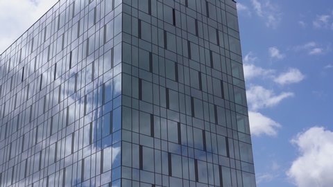 highrise commercial building with panoramic windows reflecting boundless blue sky and white clouds on summer day slow motion