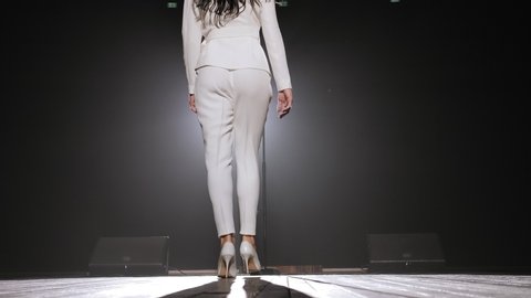 A luxurious singer in high-heeled shoes enters the stage in the light of one white spotlight. Close-up.