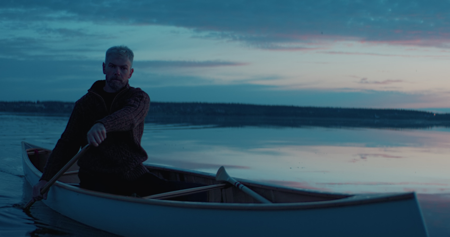 Portrait of mid 50s man canoeing alone boat on a large lake at dawn. Shot on RED cinema camera with 2x anamorphic lens
