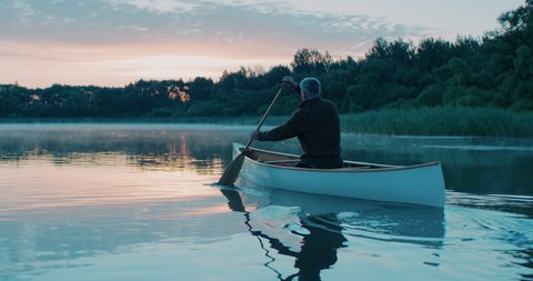 Man canoeing in a traditional wooden boat on a large lake at dawn. Shot on RED cinema camera with 2x anamorphic lens