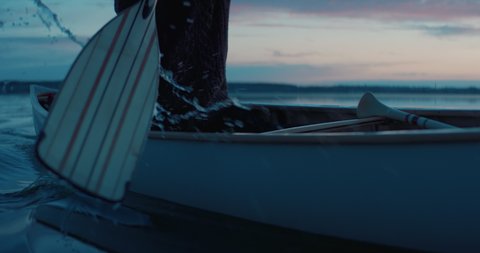 CU view of a paddle, man canoeing alone boat on a large lake at dawn. Shot on RED cinema camera with 2x anamorphic lens