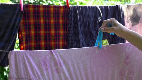 A Woman's Hand Attaches Clothespins To A Clothesline With Clean Clothes After Washing In The Backyard.
